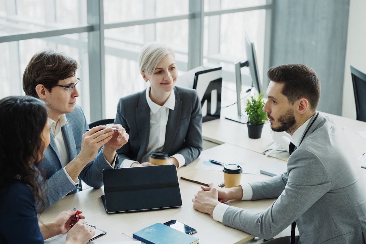 Trois professionnels en réunion de travail autour d'une table, dans un bureau lumineux.